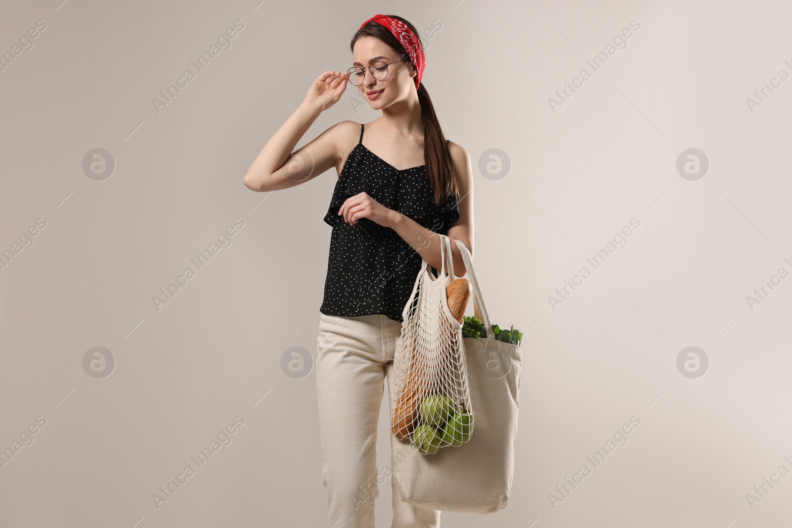 Photo of Woman with eco bags full of products on light background
