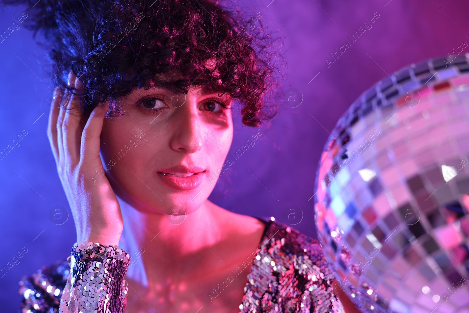 Photo of Beautiful young woman with disco ball posing on color background in neon lights