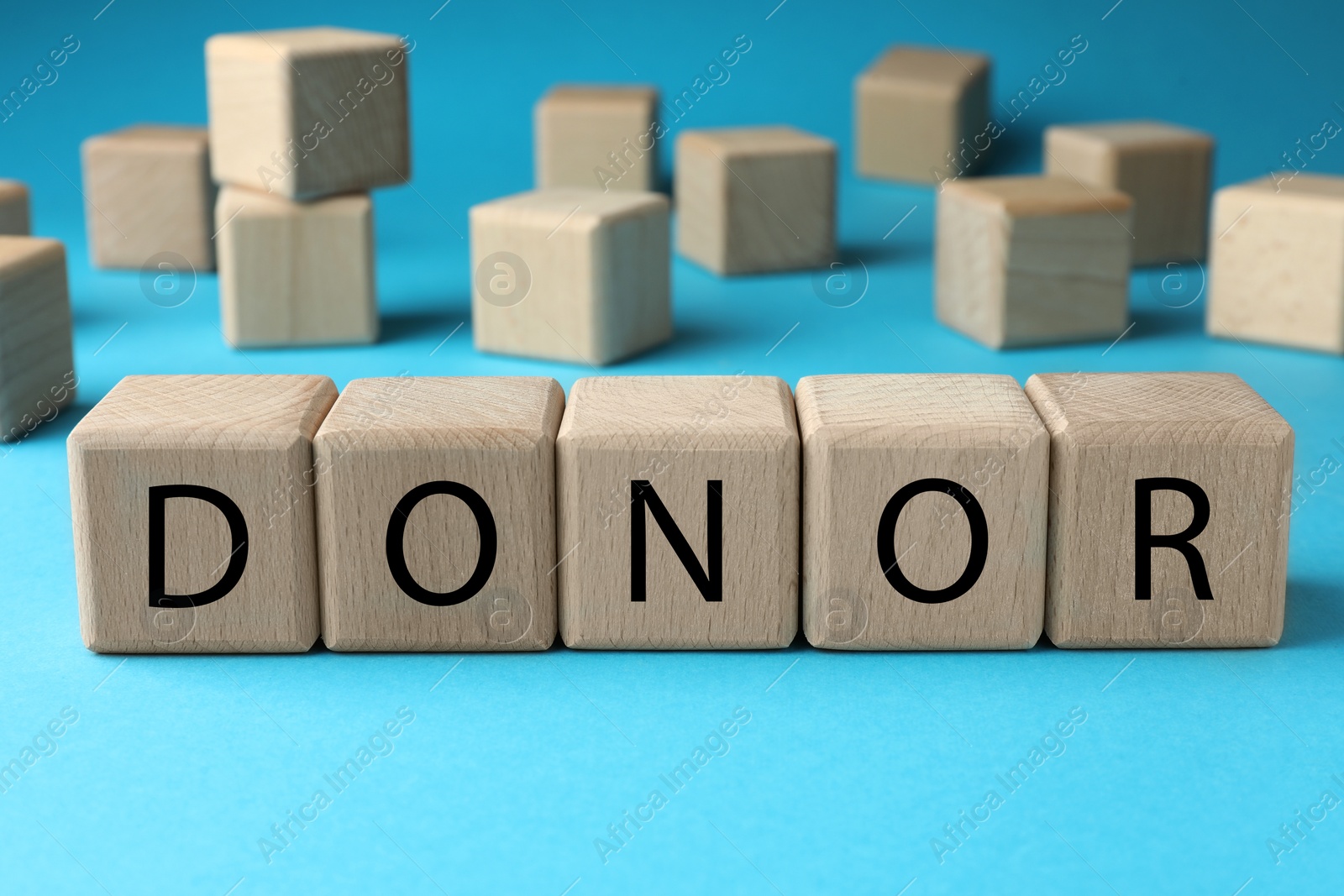 Photo of Wooden cubes with word Donor on light blue background