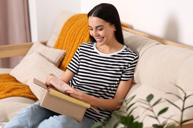 Photo of Happy young woman opening parcel on sofa at home. Internet shopping