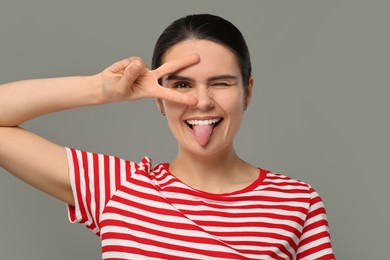 Photo of Happy young woman showing her tongue on grey background