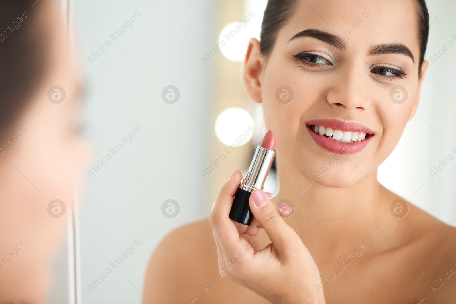 Photo of Young woman applying lipstick in front of mirror