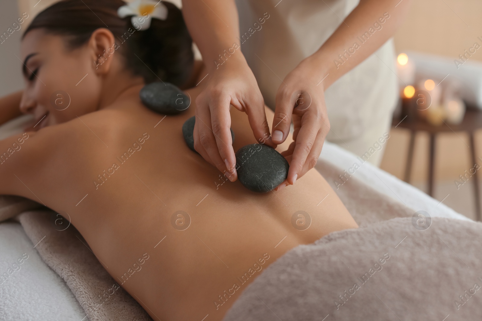 Photo of Beautiful young woman getting hot stone massage in spa salon