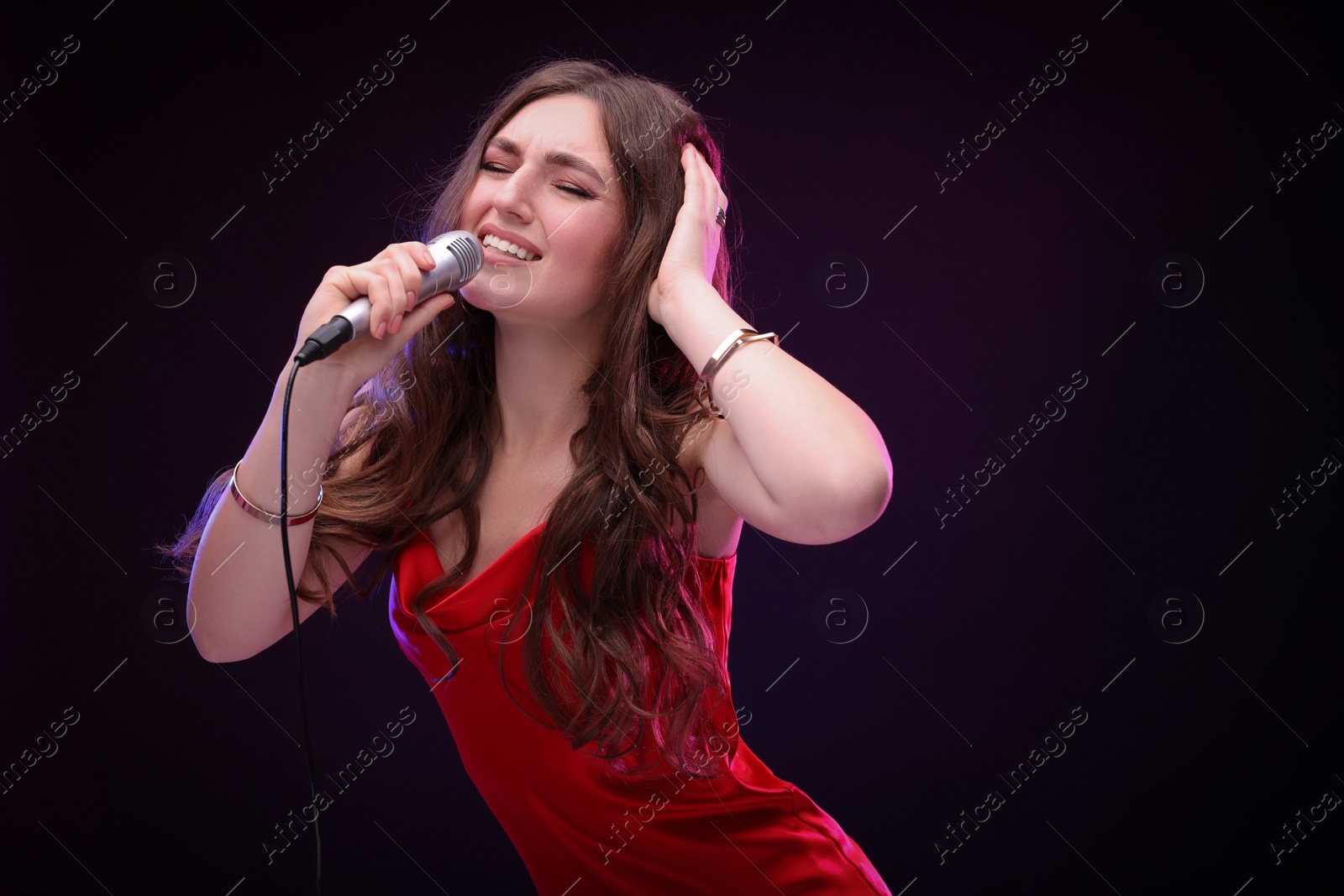 Photo of Emotional woman with microphone singing in color lights on black background. Space for text