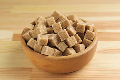 Photo of Brown sugar cubes in bowl on wooden table, closeup