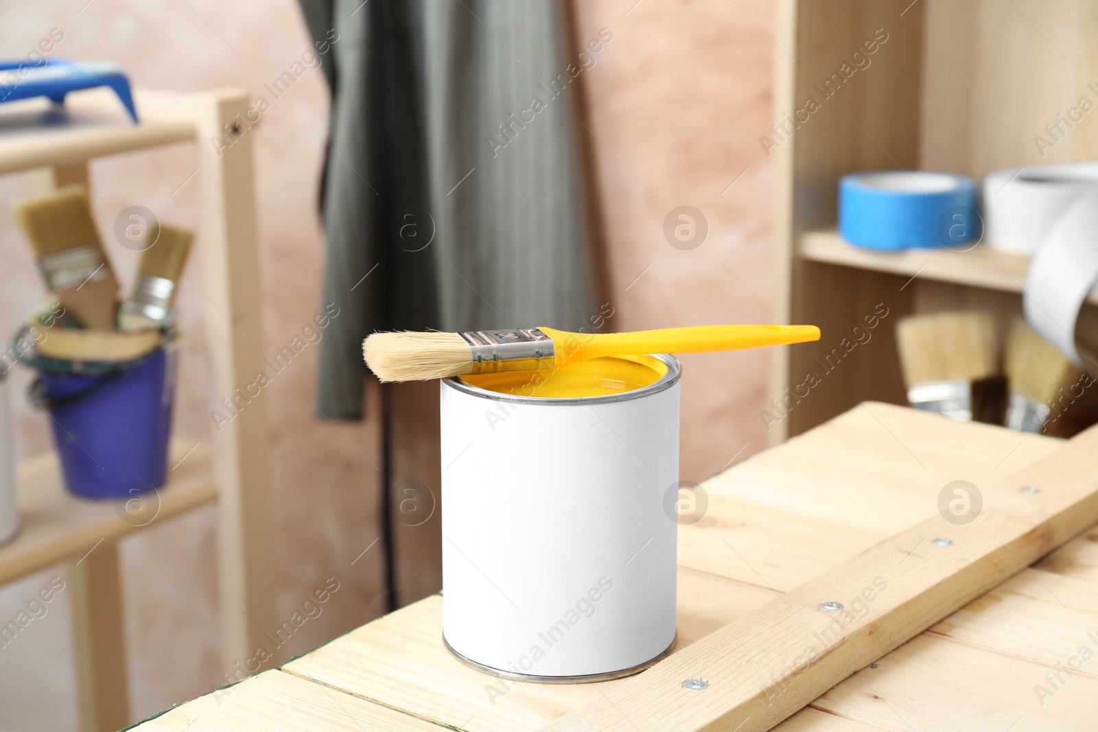 Photo of Can of yellow paint with brush on wooden table indoors