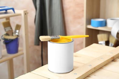 Photo of Can of yellow paint with brush on wooden table indoors