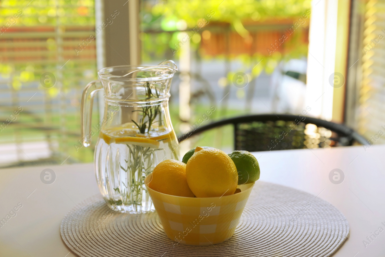 Photo of Jug with refreshing lemon water and citrus fruits in bowl on table indoors