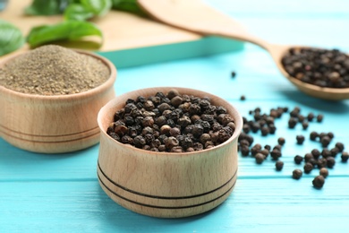 Photo of Bowls of black powdered pepper and corns on blue wooden table