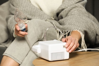 Photo of Woman using nebulizer at table indoors, closeup