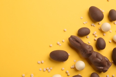 Photo of Flat lay composition with chocolate Easter bunny, eggs and candies on yellow background. Space for text