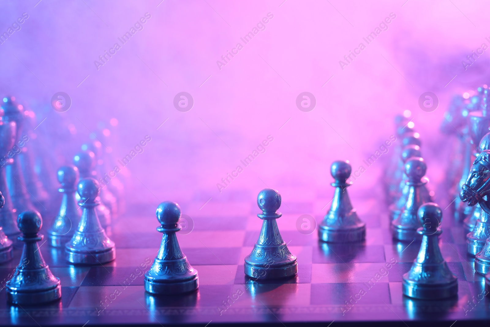 Photo of Chess pawns on checkerboard in color light, selective focus. Space for text