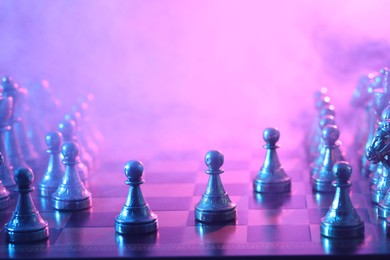 Chess pawns on checkerboard in color light, selective focus. Space for text