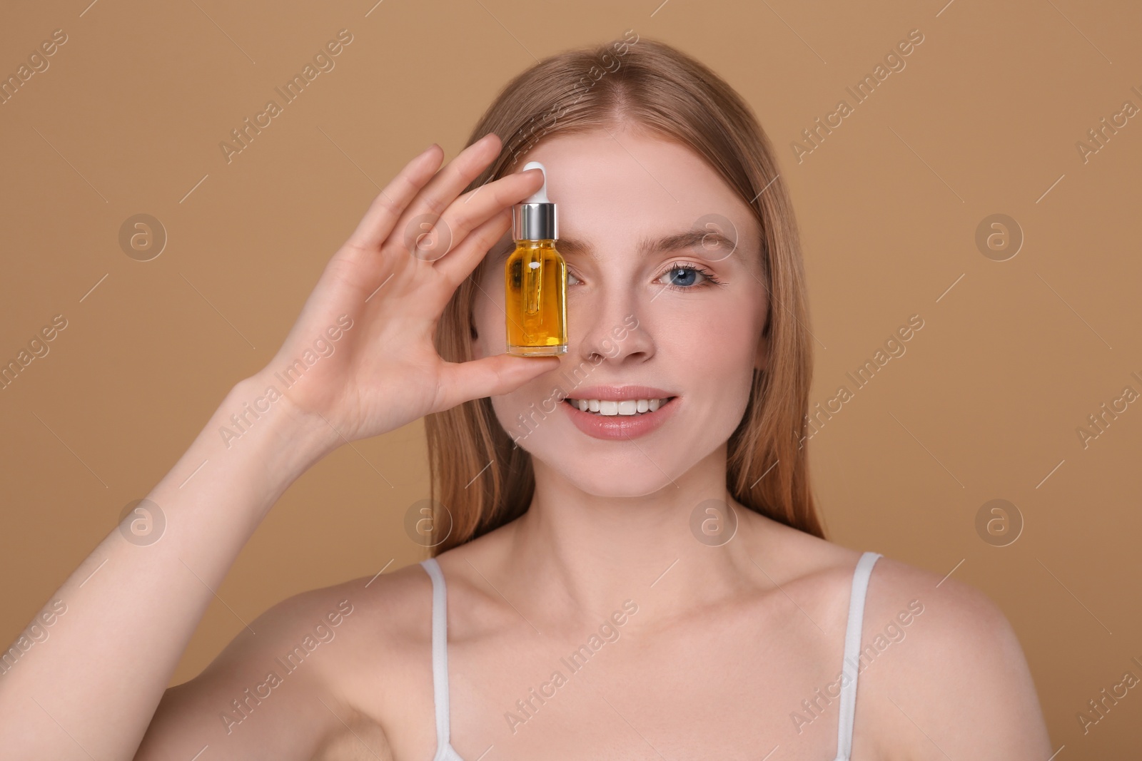 Photo of Beautiful young woman with bottle of essential oil on brown background