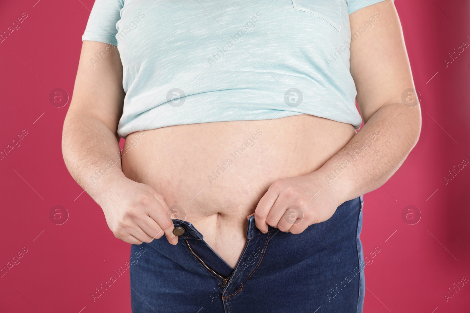 Photo of Overweight woman trying to wear tight jeans on color background, closeup