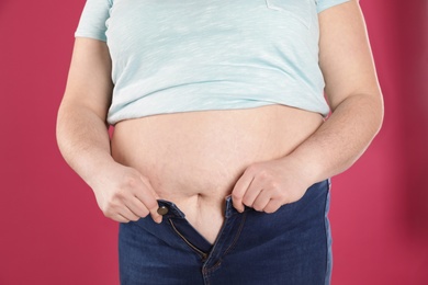 Photo of Overweight woman trying to wear tight jeans on color background, closeup