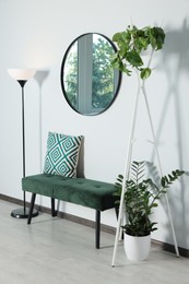 Stylish round mirror on white wall over bench in room