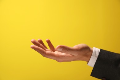 Man holding something in hand on yellow background, closeup. Space for text