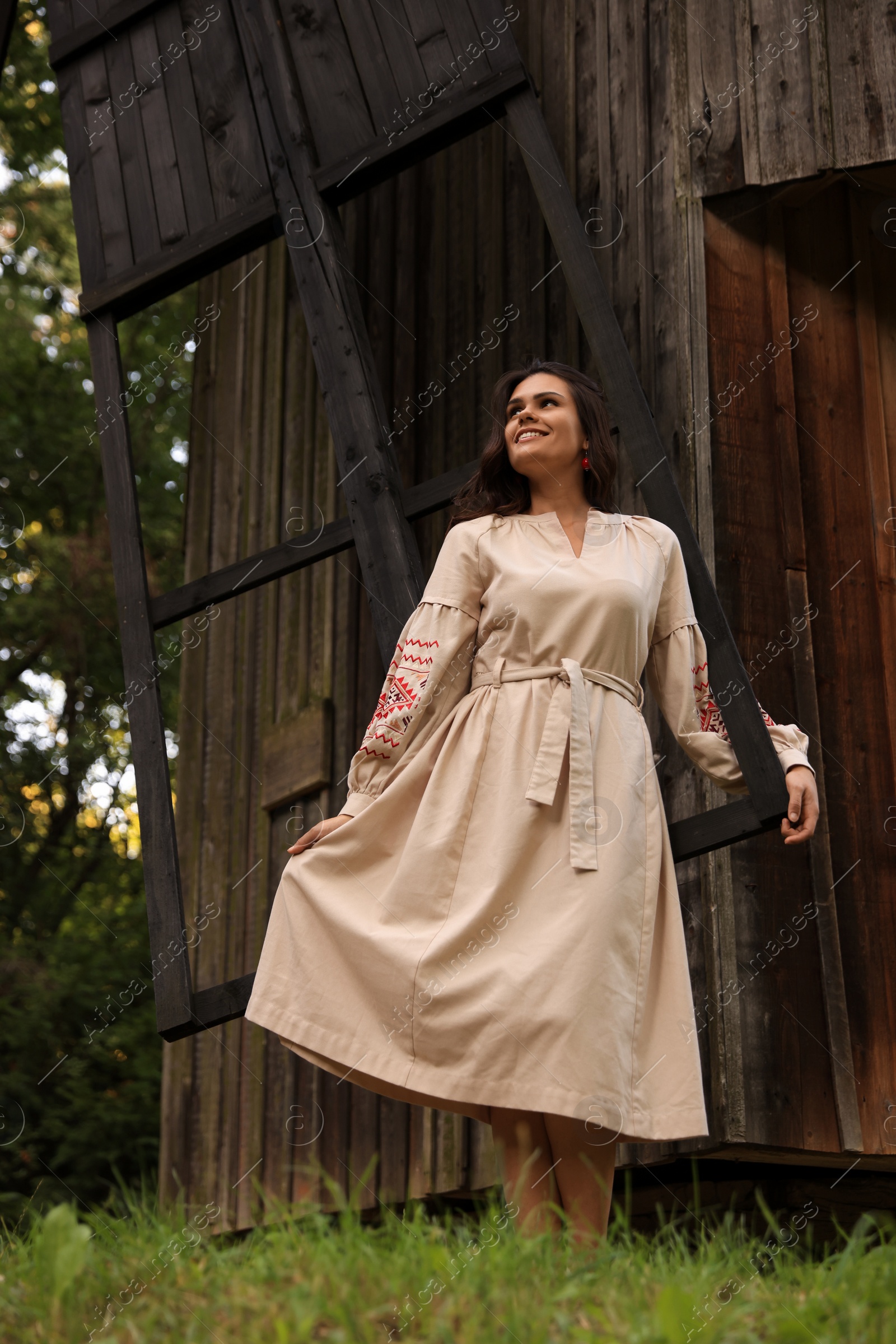 Photo of Beautiful woman wearing embroidered dress near old wooden mill in countryside. Ukrainian national clothes