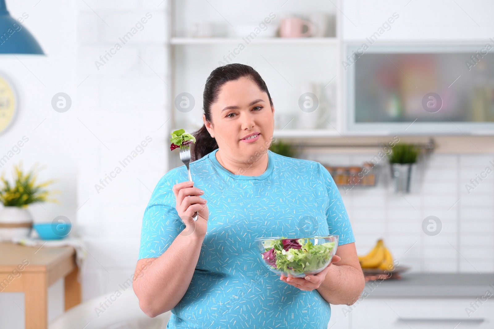 Photo of Overweight woman with bowl of salad in kitchen. Healthy diet