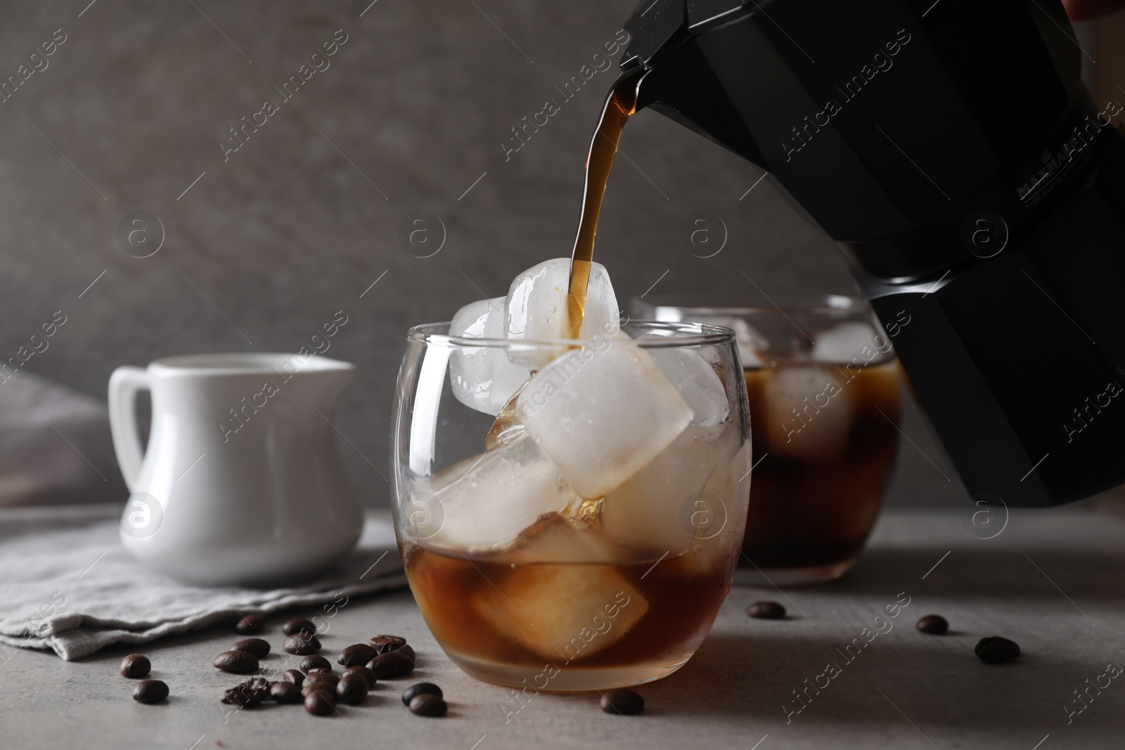 Photo of Woman pouring coffee into glass with ice cubes at gray table, closeup