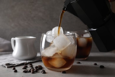 Photo of Woman pouring coffee into glass with ice cubes at gray table, closeup