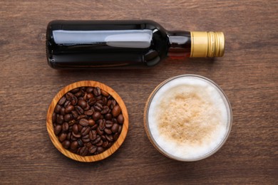 Bottle of delicious syrup, glass of coffee and beans on wooden table, flat lay