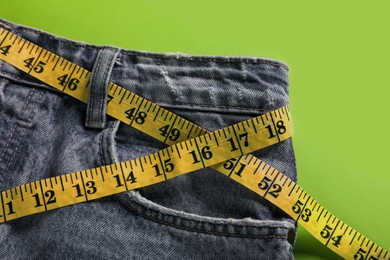 Jeans with measuring tape on green background, top view. Weight loss concept