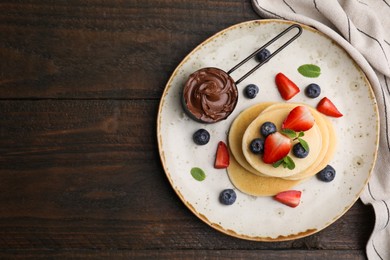 Photo of Delicious pancakes served with berries and chocolate spread on wooden table, top view. Space for text