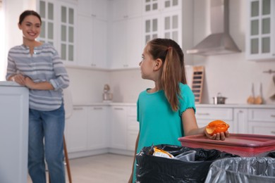 Photo of Little girl throwing tangerine peel into trash bin in kitchen. Separate waste collection