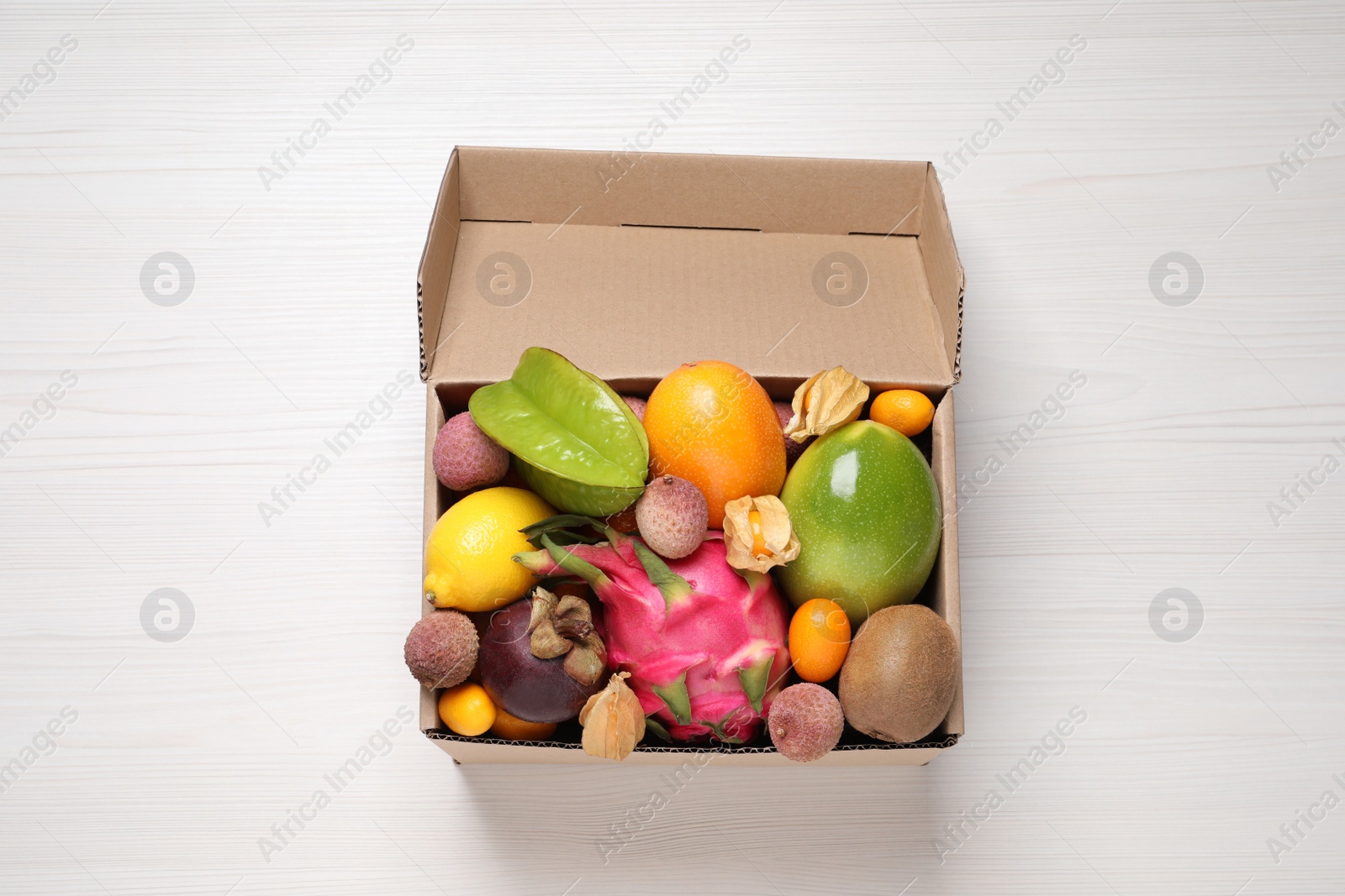 Photo of Cardboard box with different exotic fruits on white wooden table, top view