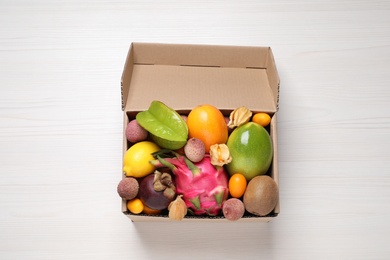 Cardboard box with different exotic fruits on white wooden table, top view
