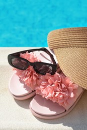 Photo of Stylish visor cap, slippers and sunglasses near outdoor swimming pool on sunny day, closeup