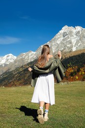 Photo of Young woman walking in beautiful mountains on sunny day, back view
