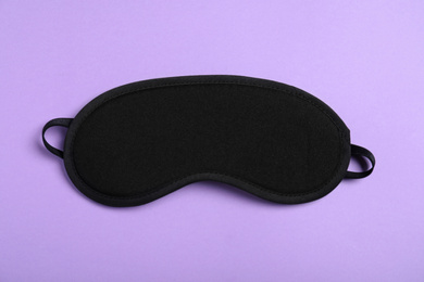 Photo of Black sleeping mask on violet background, top view. Bedtime accessory