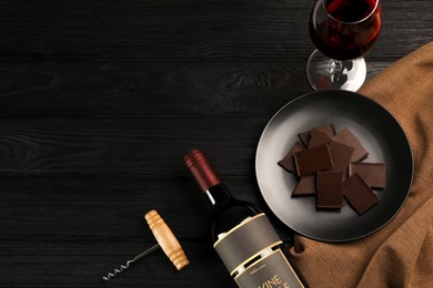 Photo of Flat lay composition with tasty red wine and chocolate on black wooden table. Space for text