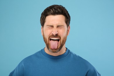 Photo of Man showing his tongue on light blue background