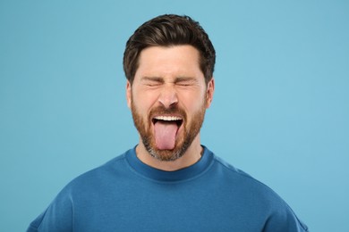 Man showing his tongue on light blue background