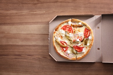 Cardboard box with tasty pizza on wooden background, top view with space for text