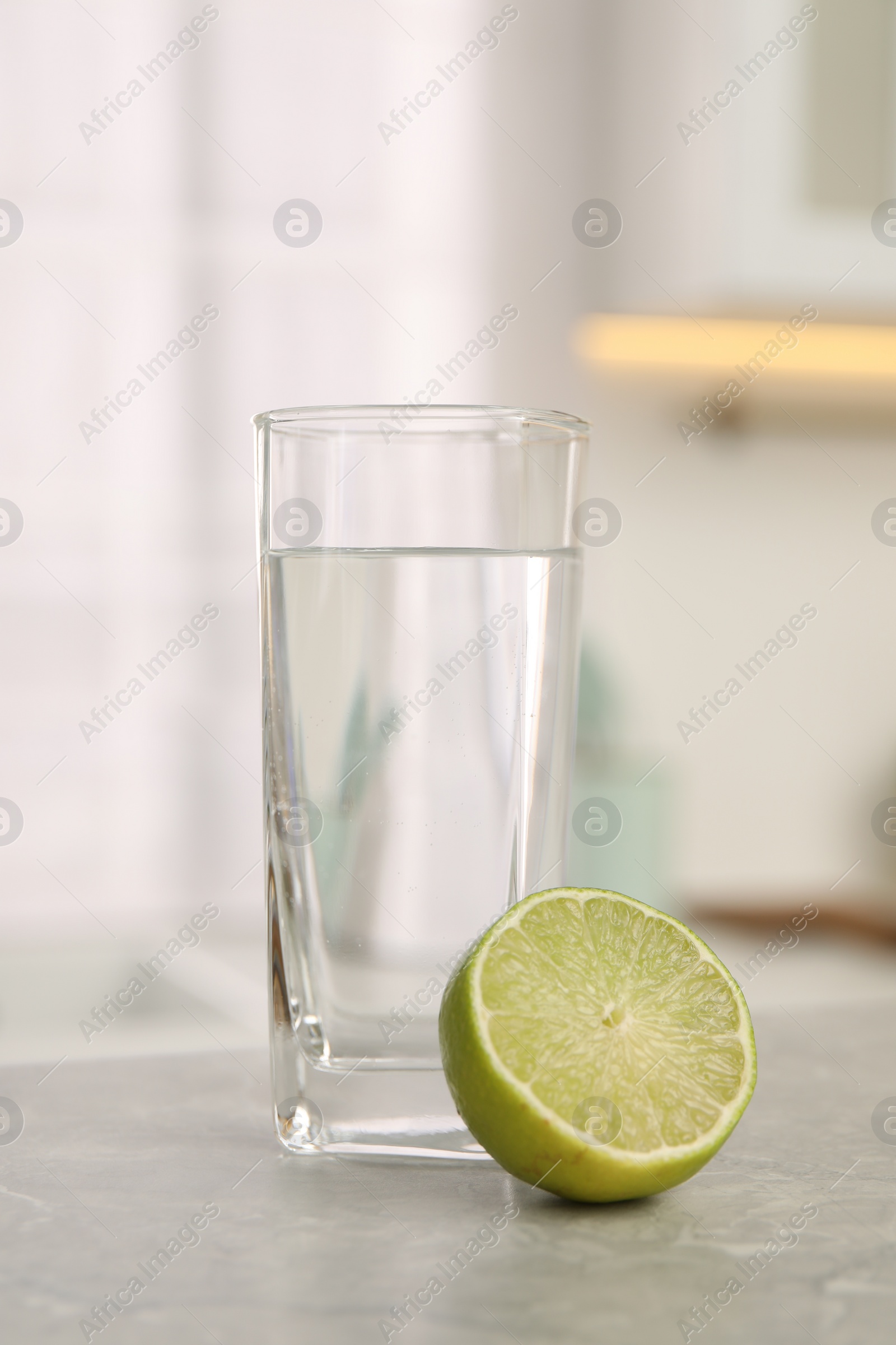 Photo of Filtered water in glass and lime on light table in kitchen, closeup