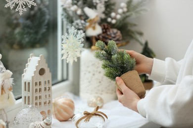 Woman holding small Christmas tree near window sill indoors, closeup