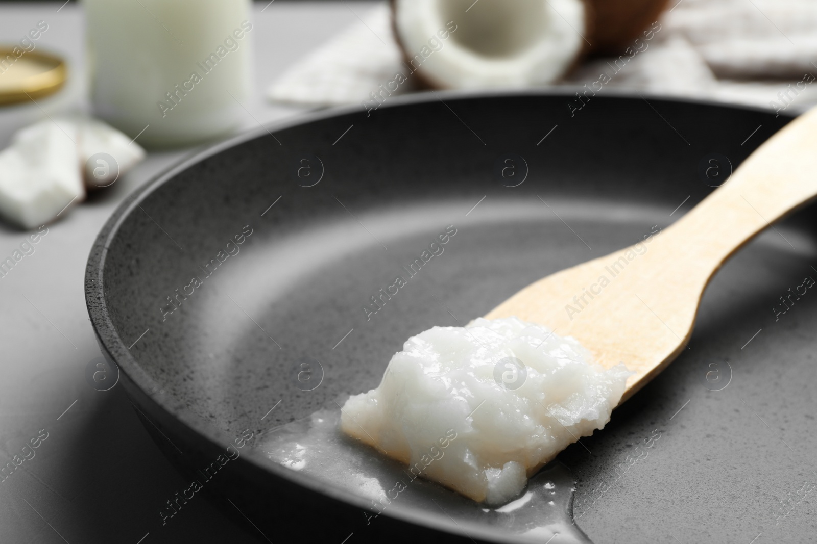 Photo of Frying pan with coconut oil and wooden spatula on grey table, closeup. Healthy cooking