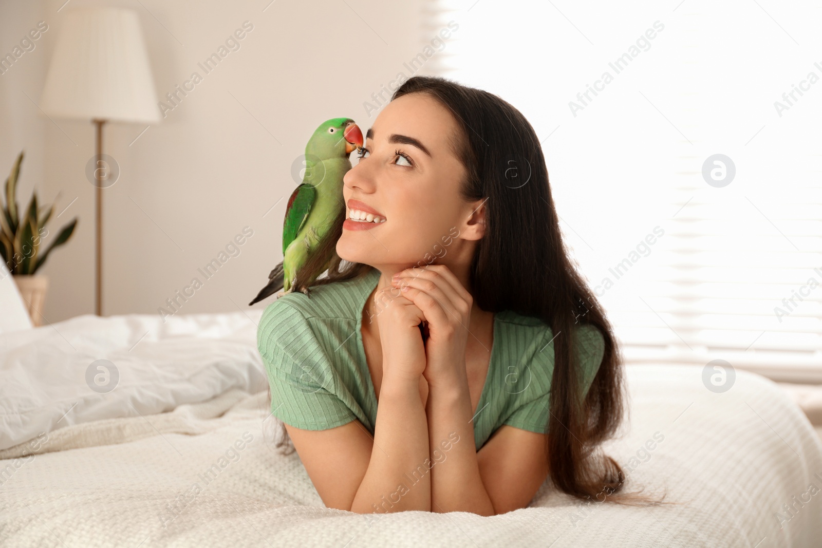 Photo of Young woman with Alexandrine parakeet indoors. Cute pet