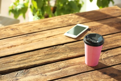 Photo of Cardboard cup of coffee and mobile phone on wooden table
