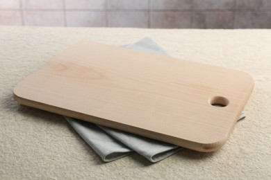 Photo of Wooden cutting board and napkin on beige table, closeup