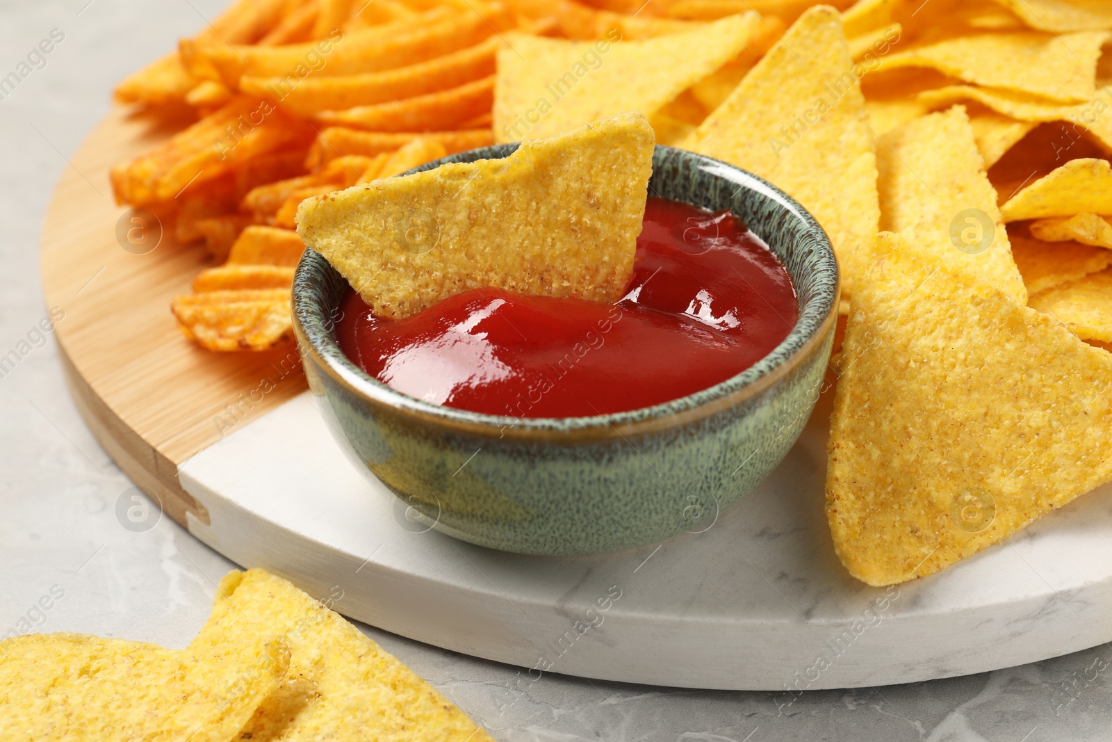 Photo of Tasty ketchup with ridged and tortilla chips on grey table, closeup