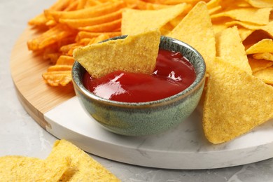 Photo of Tasty ketchup with ridged and tortilla chips on grey table, closeup