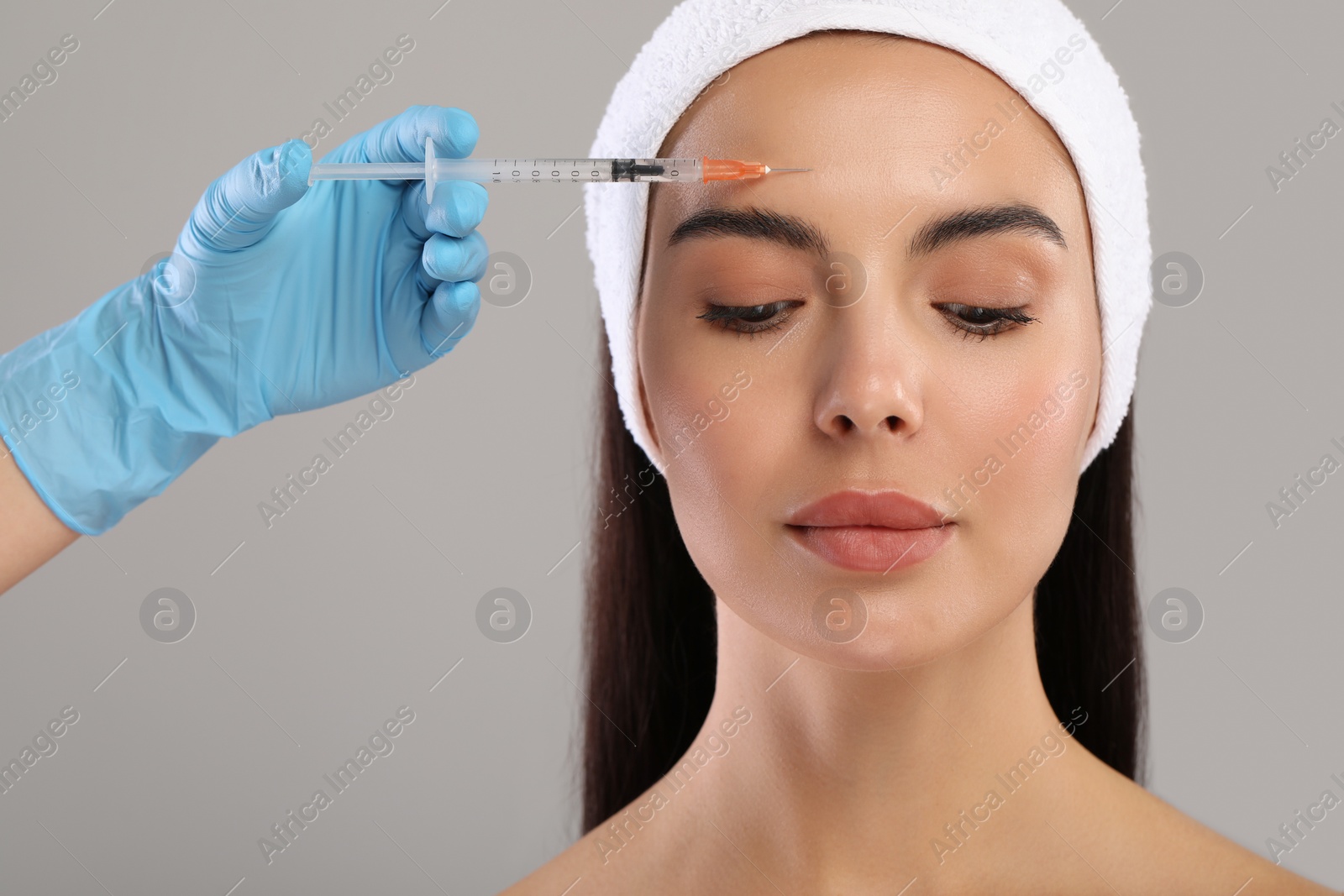 Photo of Doctor giving facial injection to young woman on light grey background. Cosmetic surgery