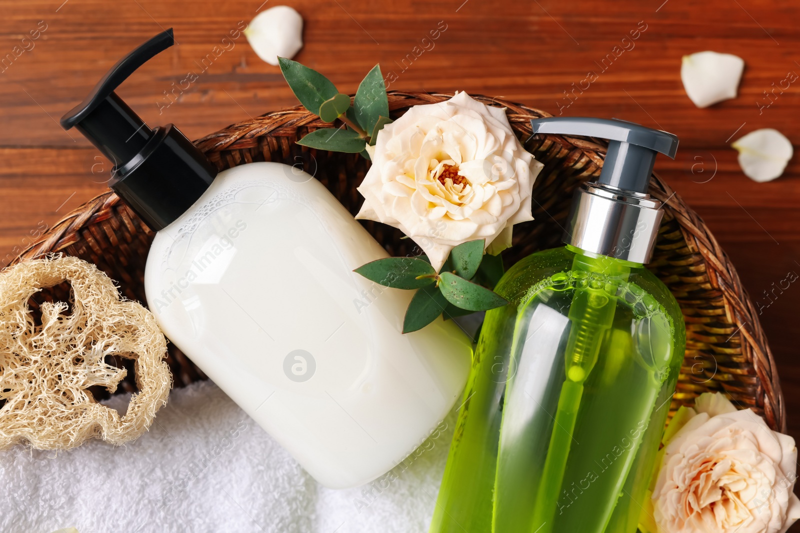 Photo of Dispensers of liquid soap, towel and roses in wicker basket on wooden table, top view