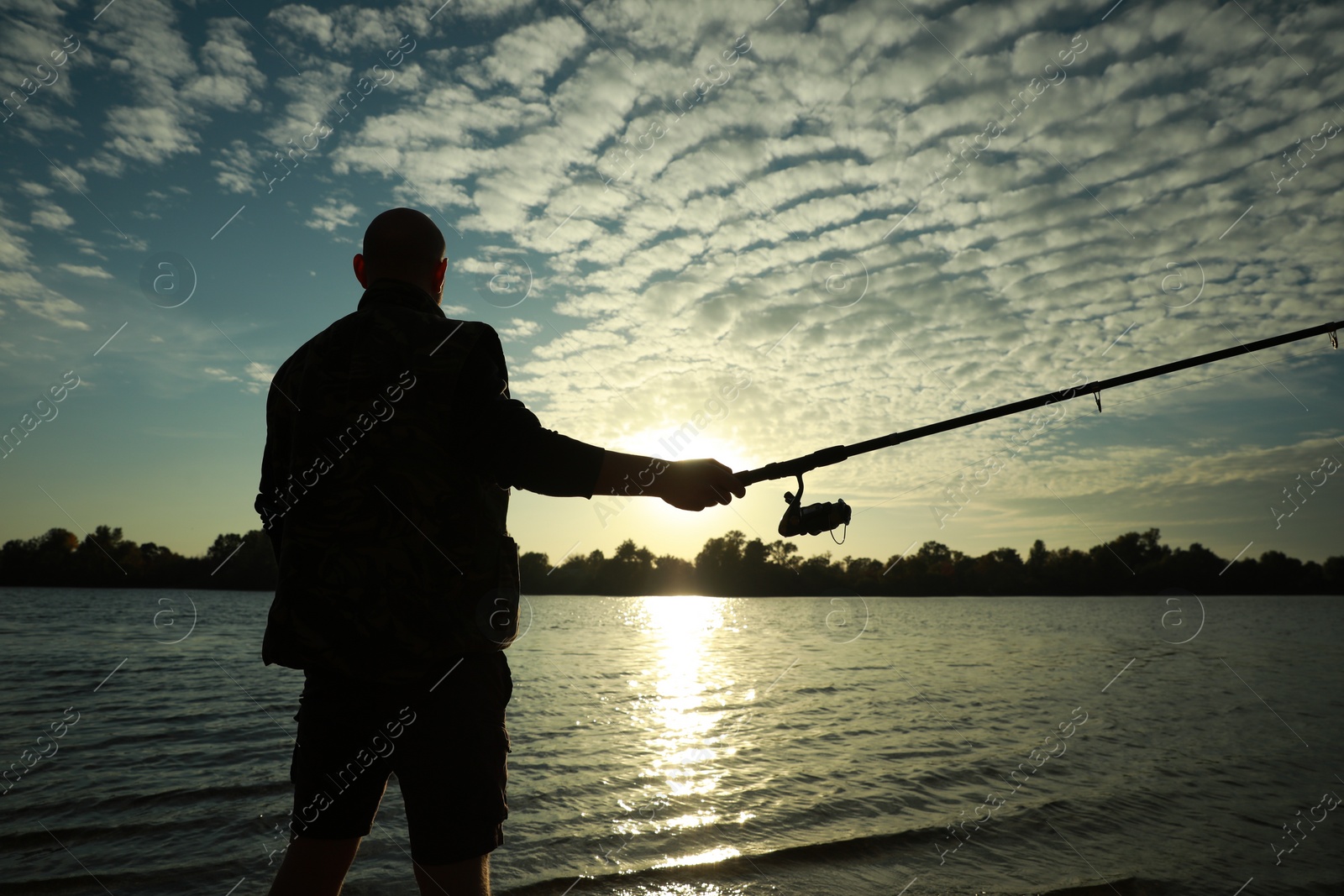 Photo of Fisherman with rod fishing at riverside at sunset, back view